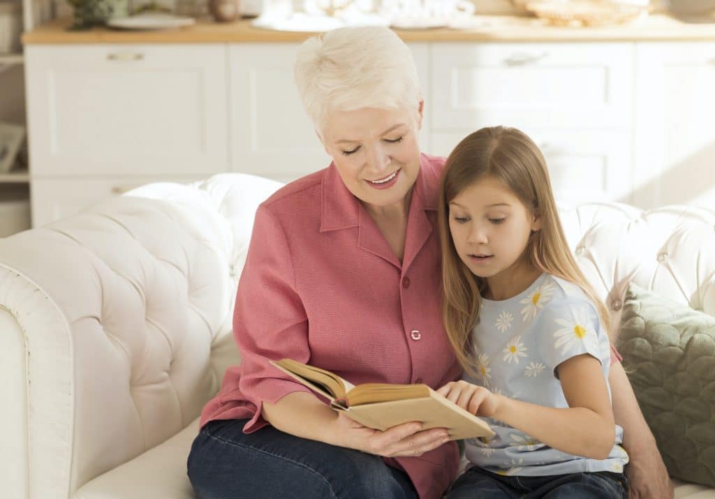 Elderly lady and her granddaughter with interesting book on sofa at home